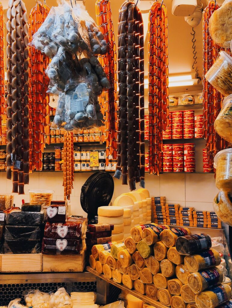 A Brazilian mercearia stall in Belo Horizonte displaying cheeses, cured meats and traditional sweets, with prices in Reais.